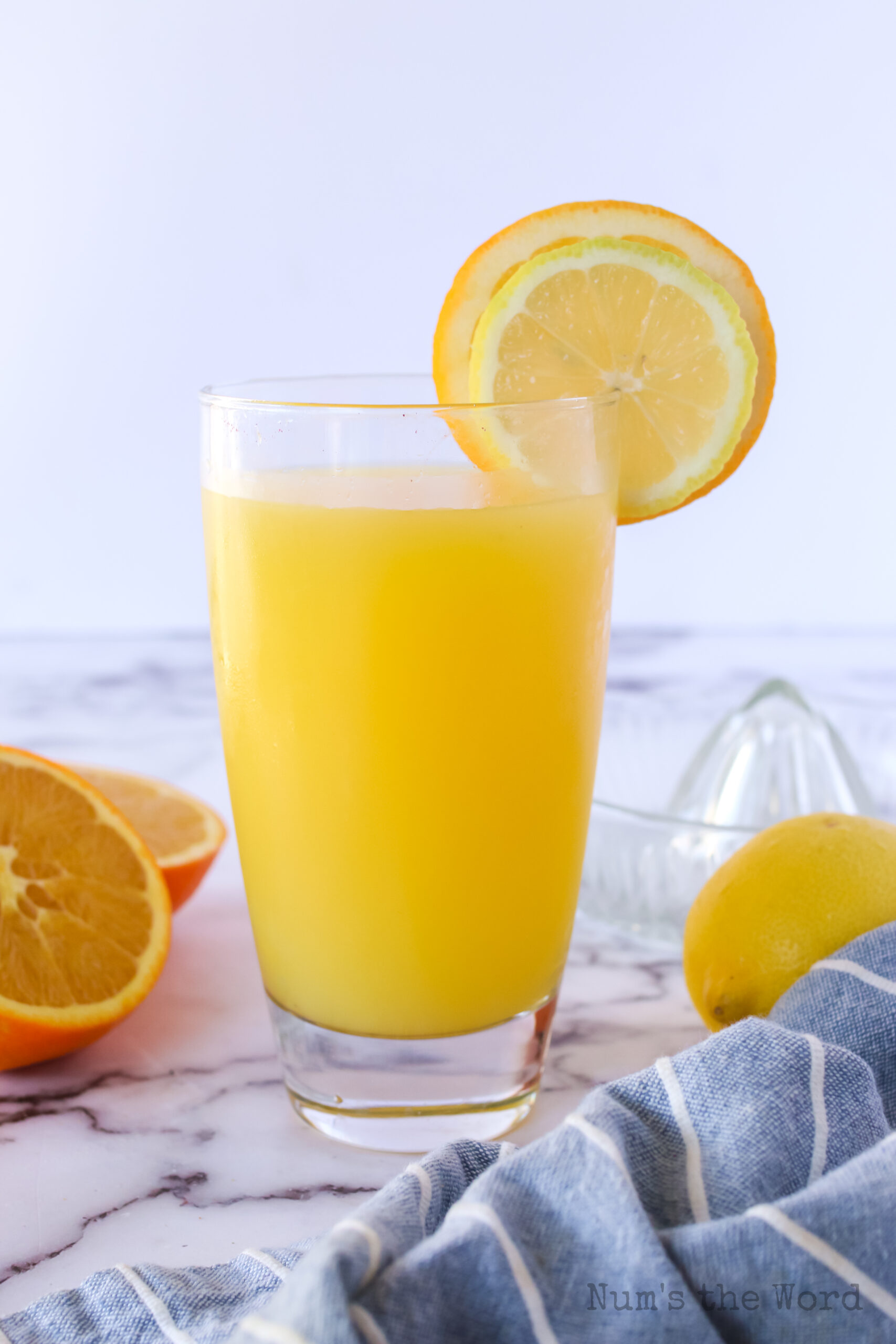 zoomed out image of glass of orange lemonade with a slice of orange and slice of lemon on the edge.