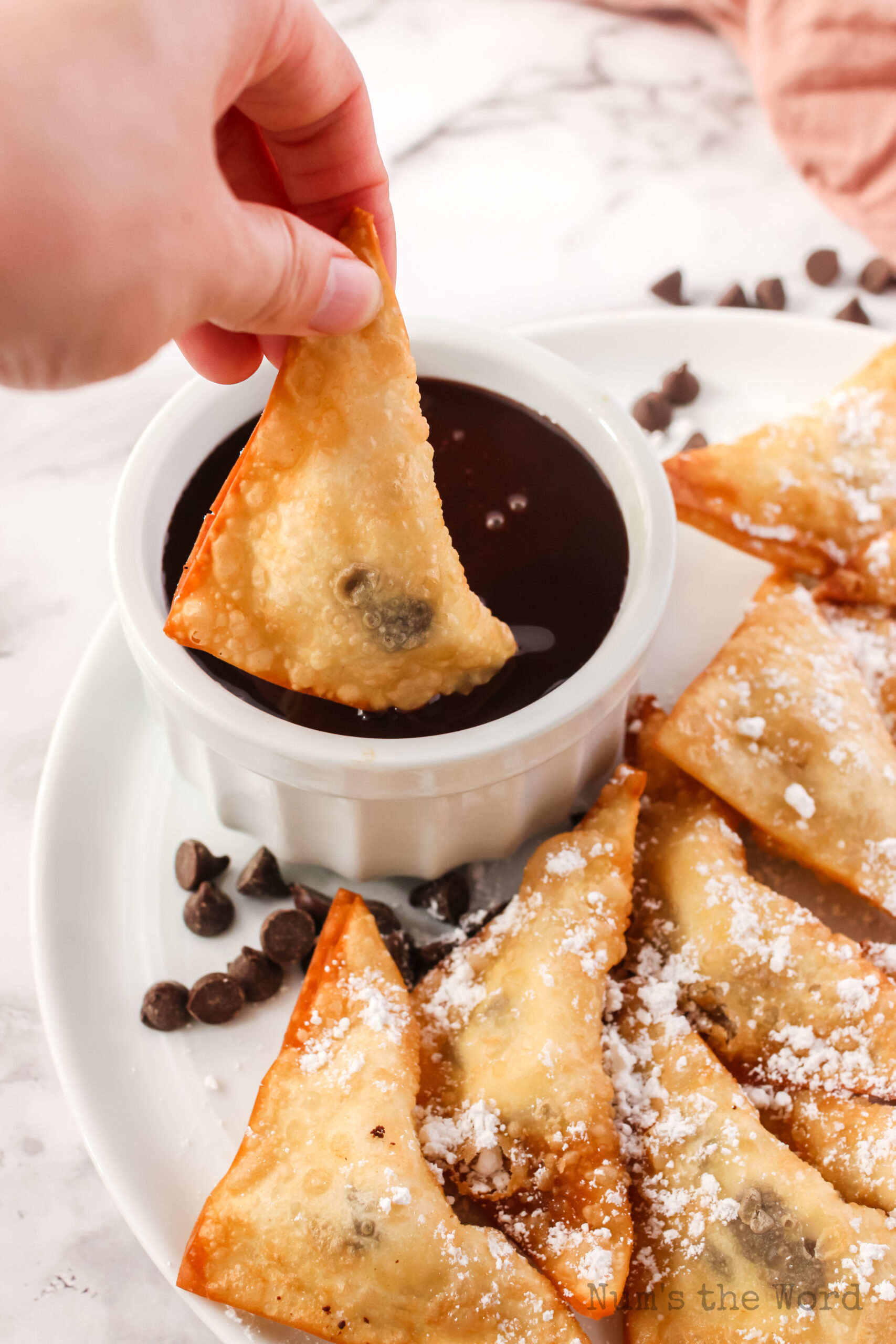 hand holding a dessert wonton and dipping it into chocolate sauce