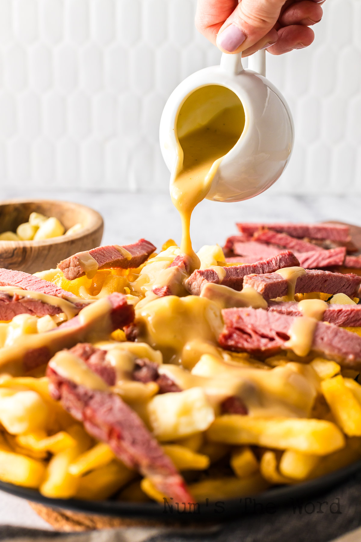 gravy being poured on top of fries, curds and corned beef.