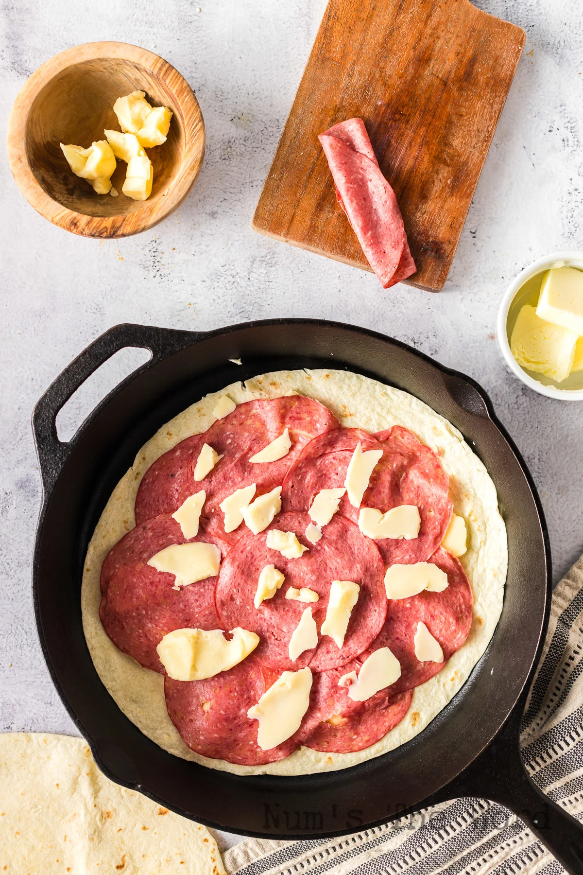 tortilla in skillet with a bottom layer of cheese curds, corned beef and top layer of cheese curds.