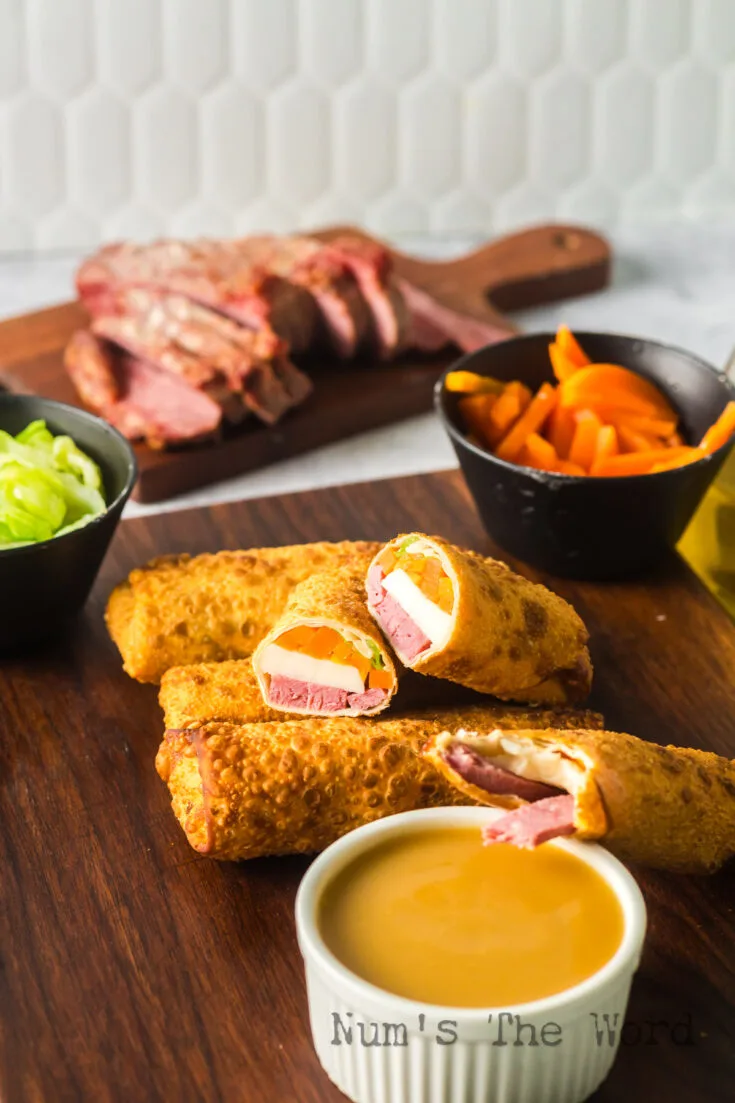 zoomed out image of eggrolls on serving tray with one cut in half and a dipping sauce in front.