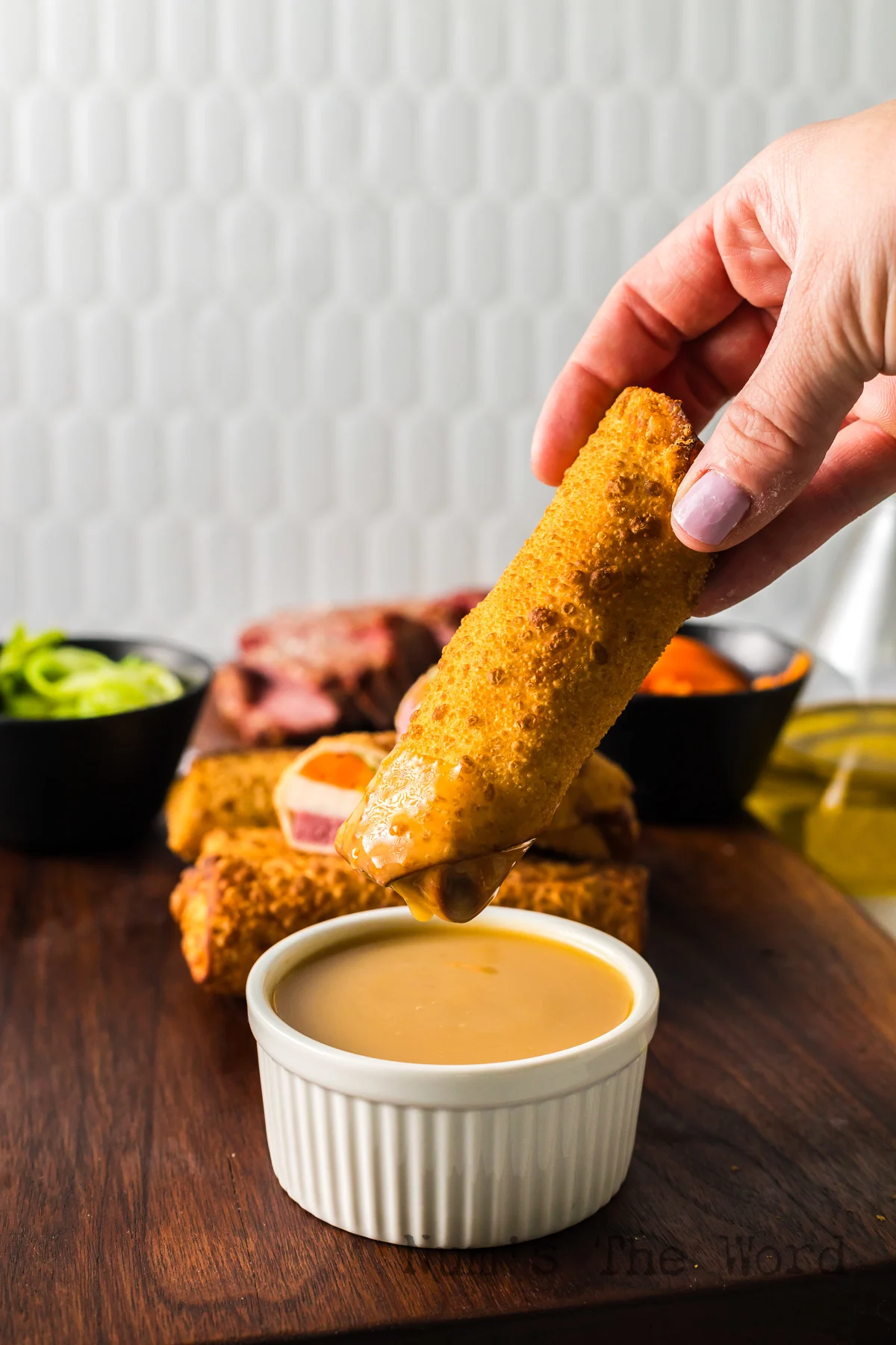 Hand holding an egg roll and dipping it into a yummy sauce.