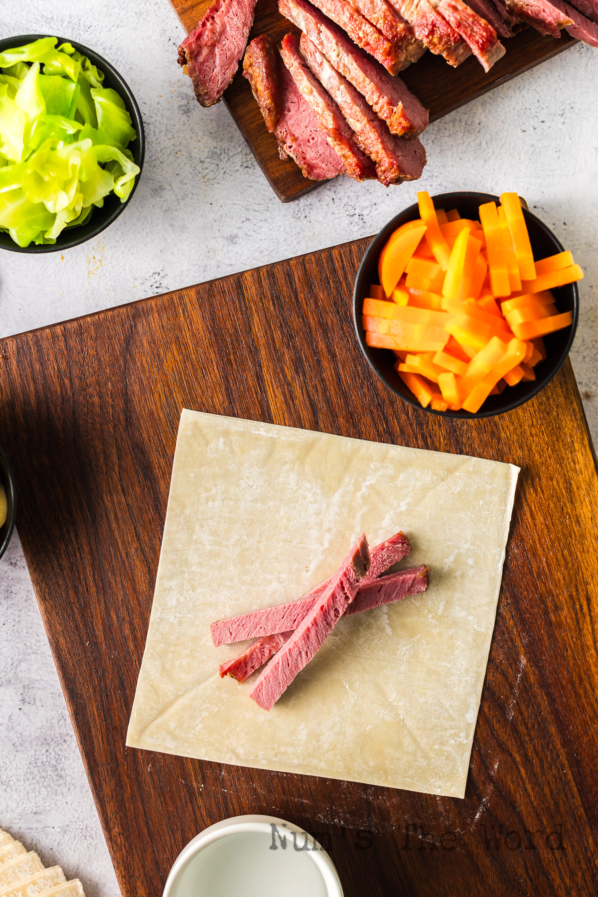 Egg roll wrapper laid out on cutting board with a few slices of corned beef on top.