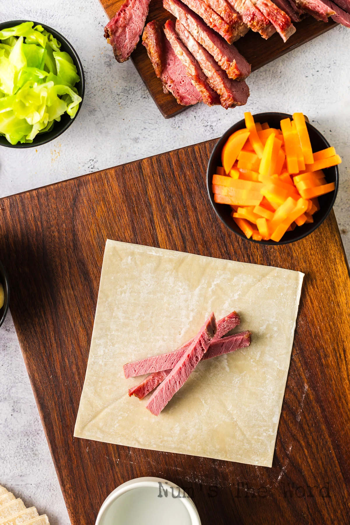 Egg roll wrapper laid out on cutting board with a few slices of corned beef on top.