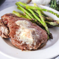 single steak on a plate with garlic butter on top and asparagus on the side