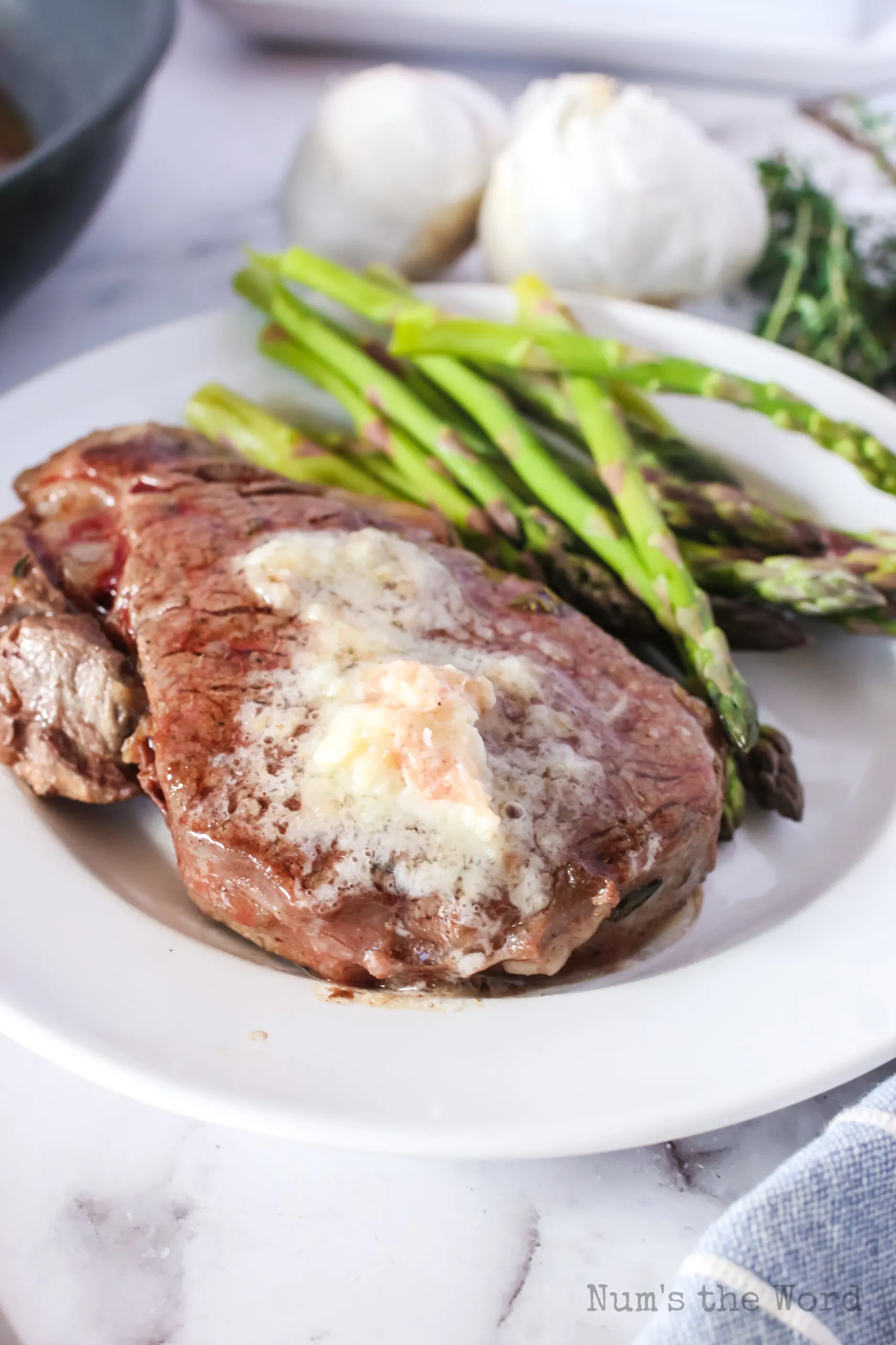 single steak on a plate with garlic butter on top and asparagus on the side