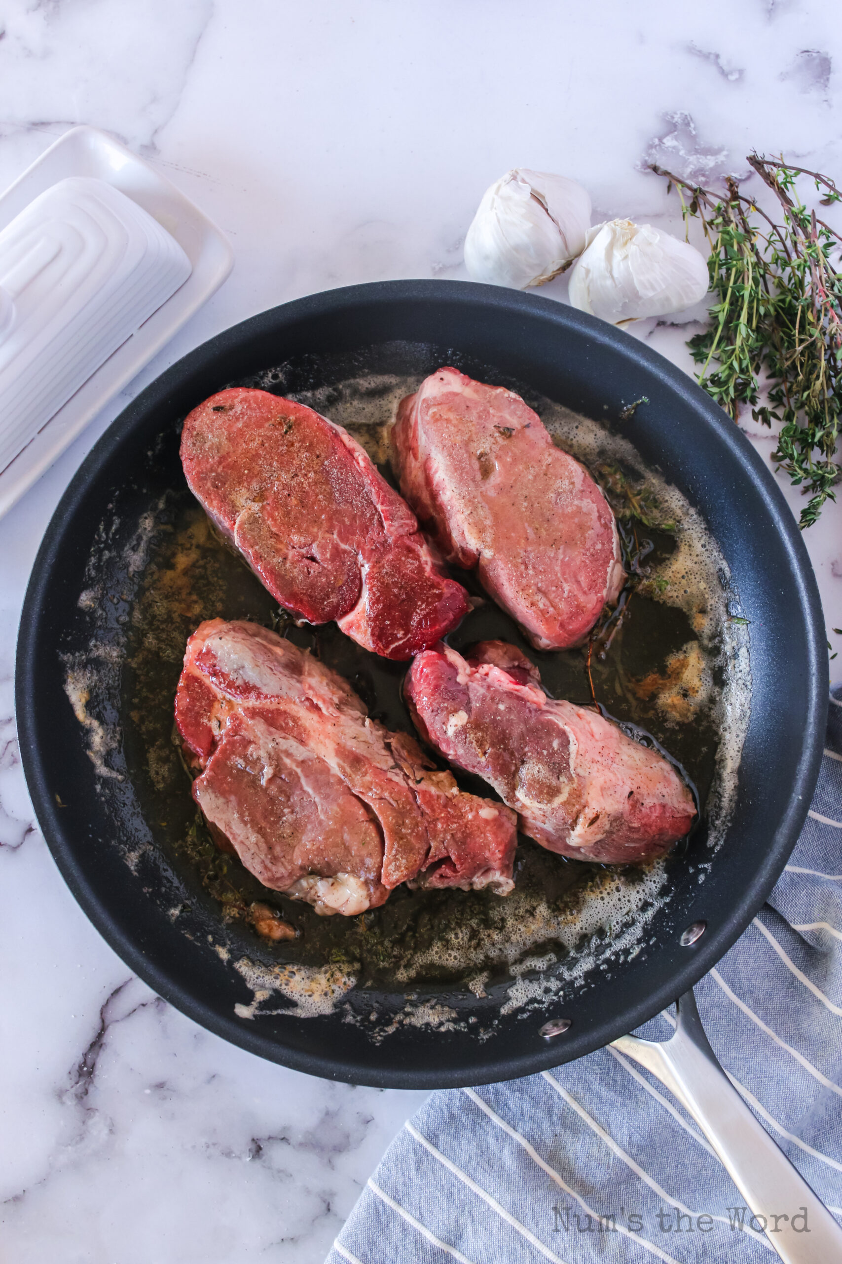 4 filet mignon steaks in a skillet cooking in garlic butter