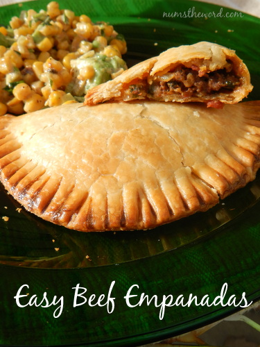 Easy Beef Empanadas - Main image for recipe - 1 full cooked empanada on plate with a broken open empanada half on top to show filling. Corn salad in the background.