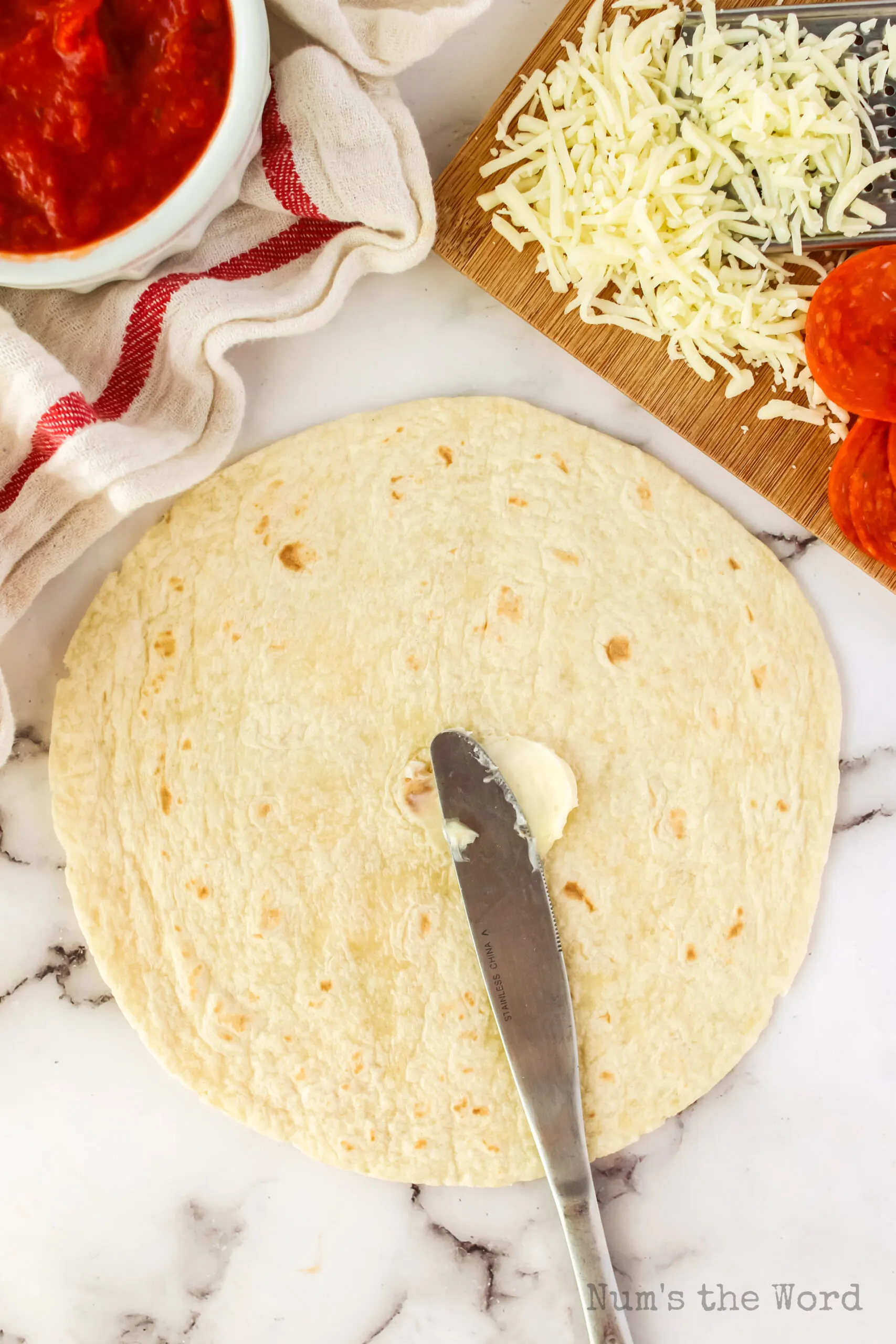 knife buttering one side of a tortilla