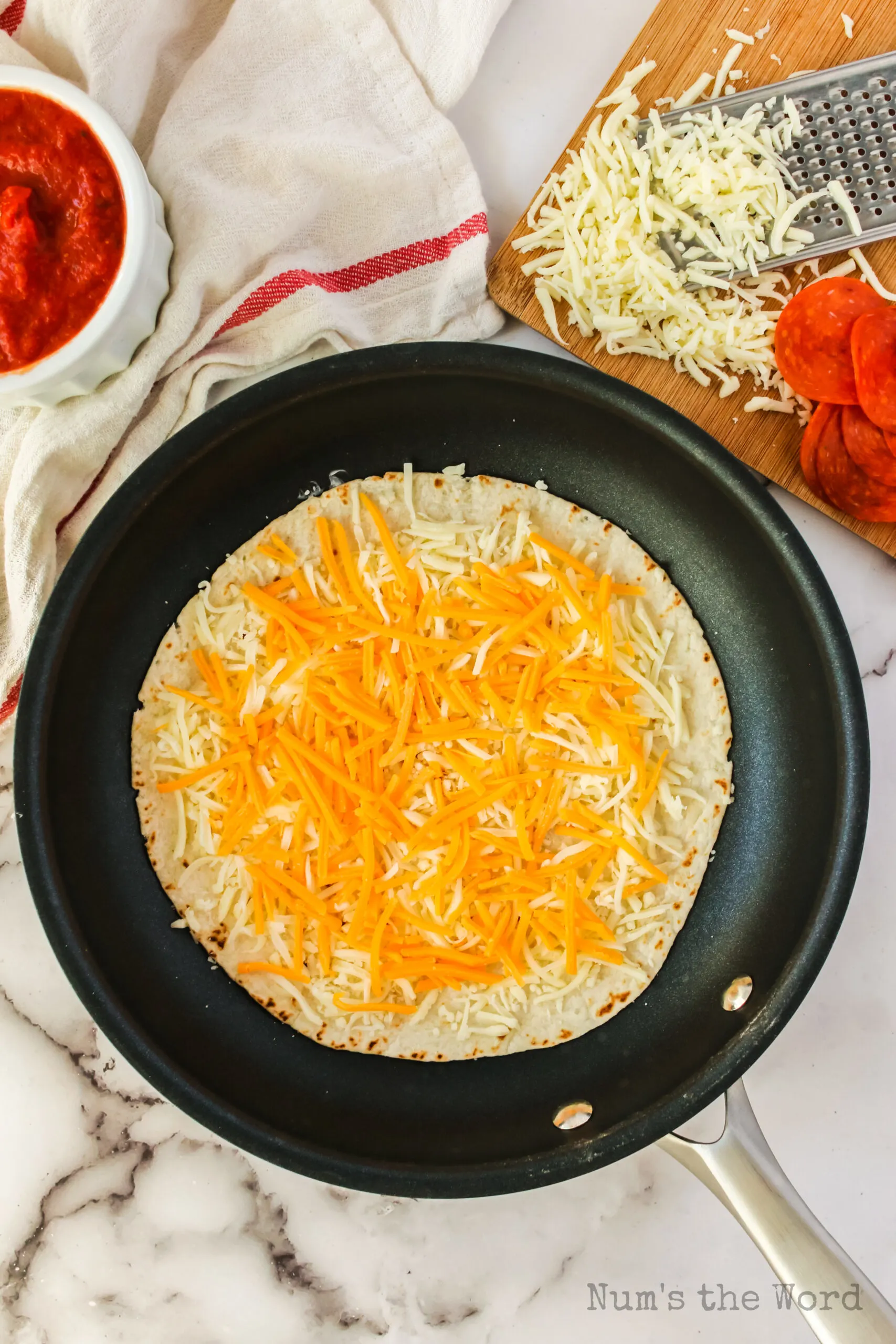 A buttered tortilla in a skillet with cheese on top.
