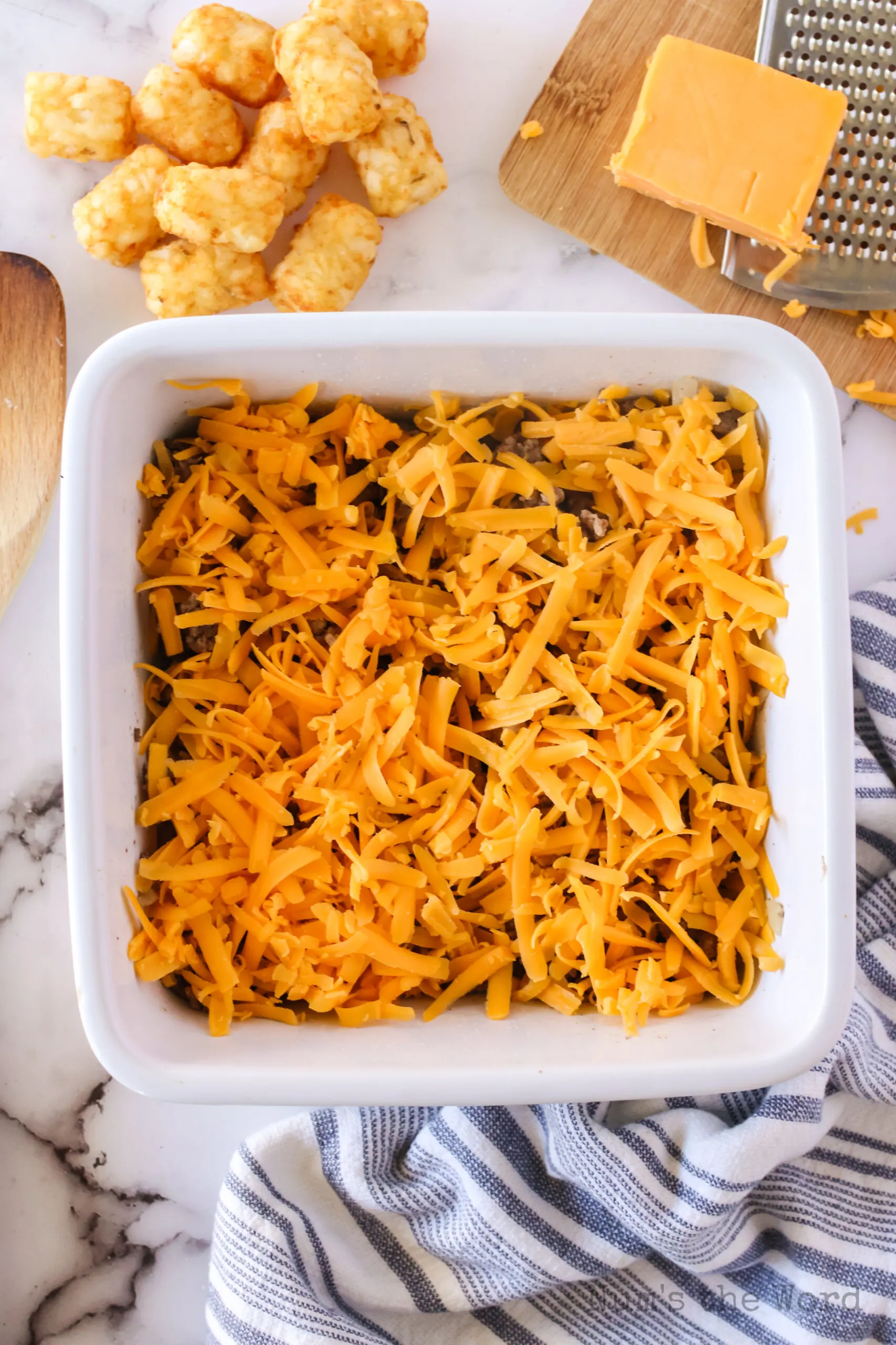 shredded cheddar cheese on top of ground beef mixture in casserole dish