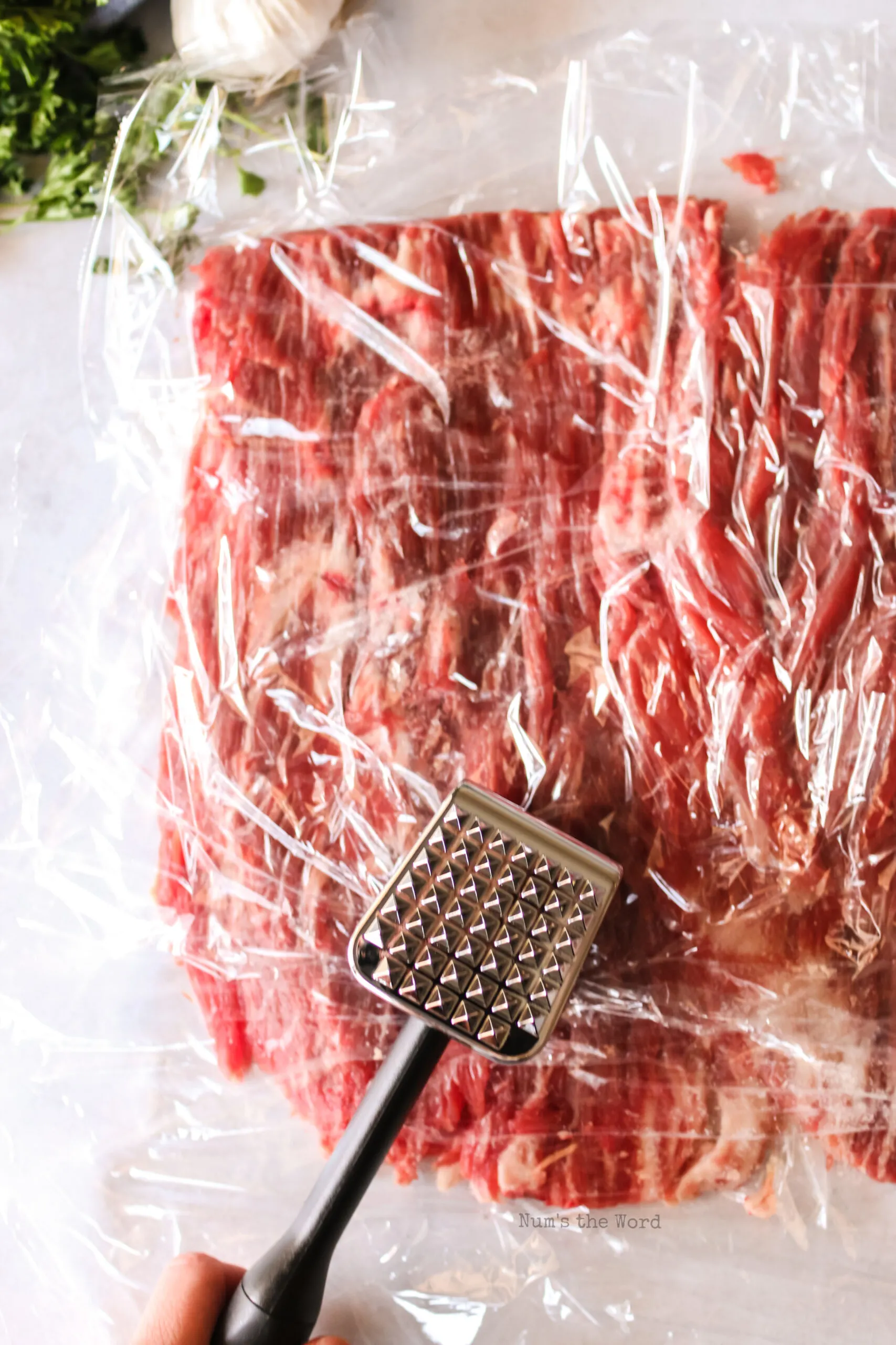Plastic wrap laid over steak with a meat hammer pounding meat to even it out.