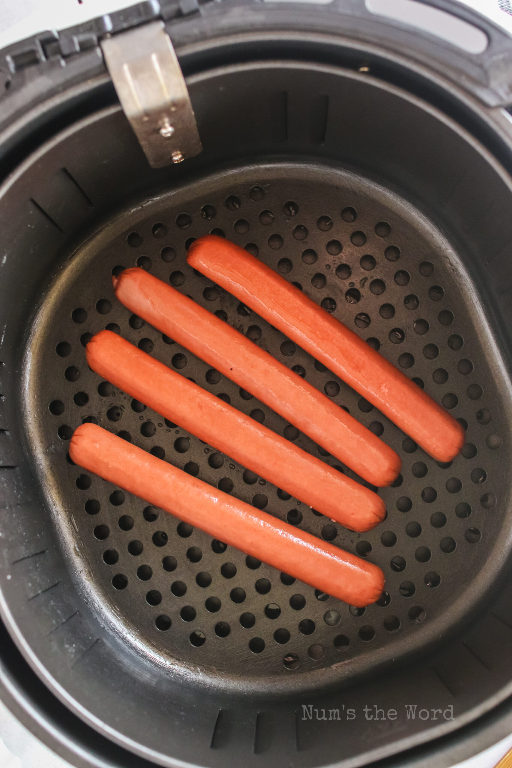 4 hot dogs placed into the air fryer, uncooked.
