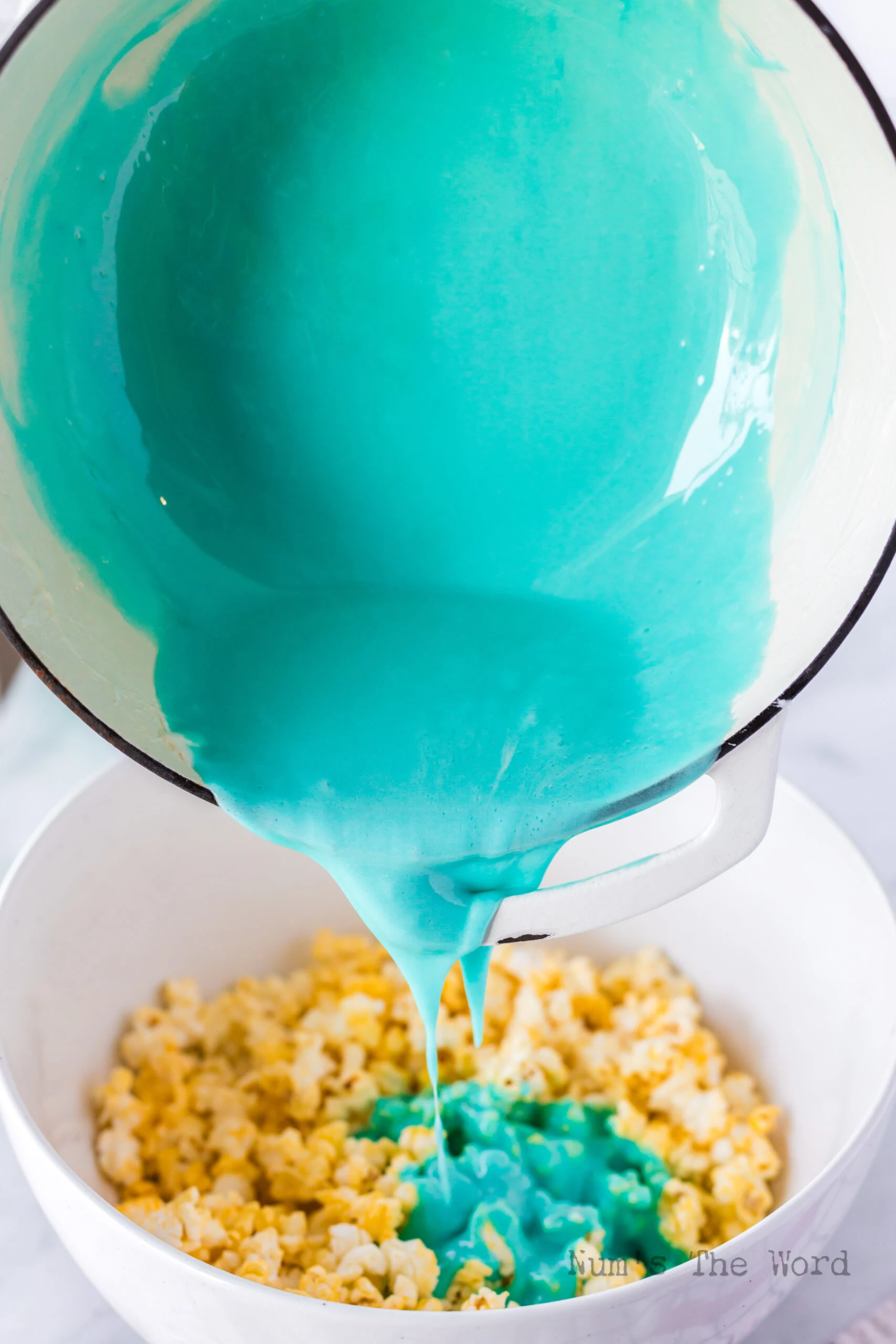 Melted blue marshmallow mixture being poured over popcorn