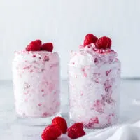 side view of two jars of raspberries and whipped cream