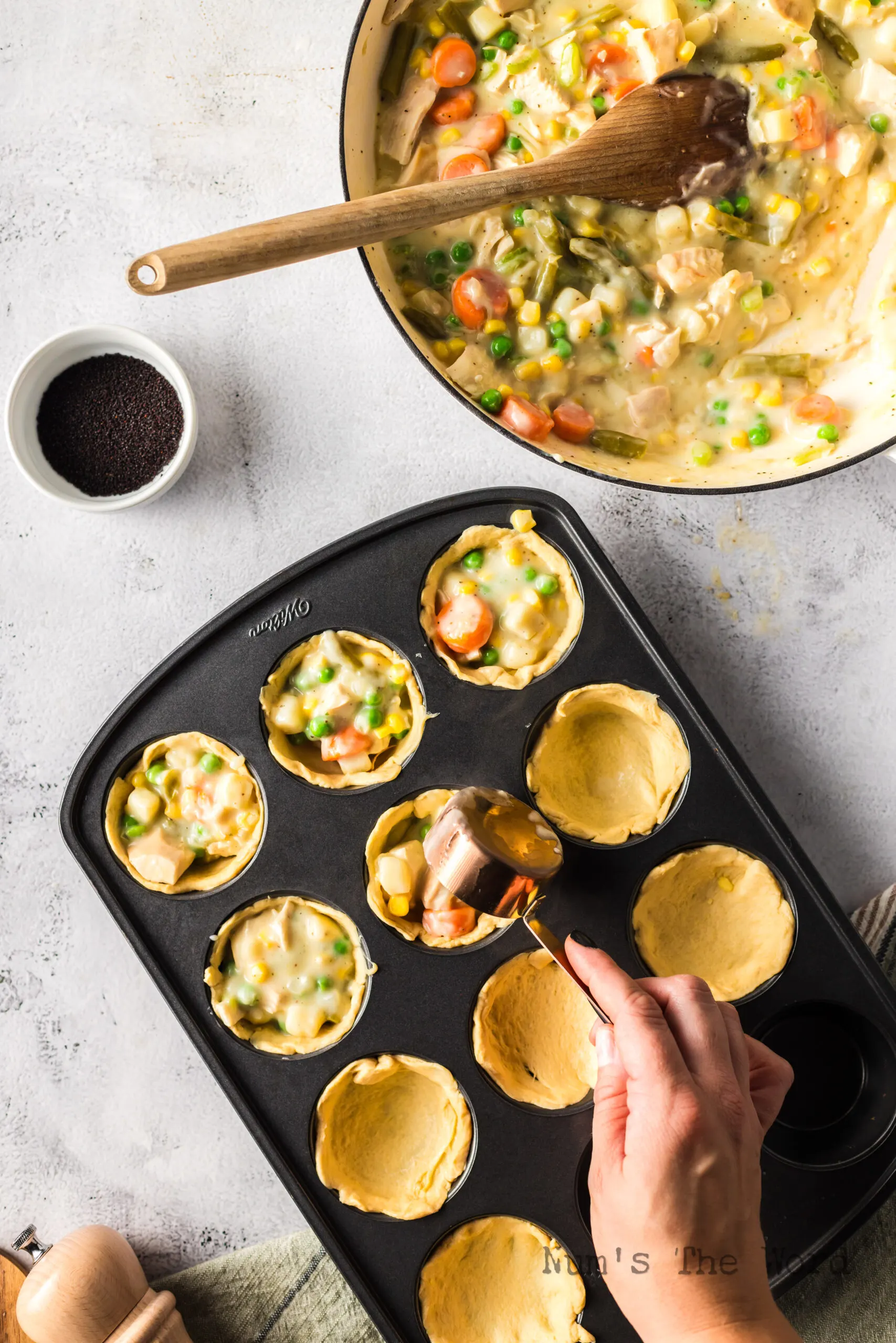 half biscuits placed in 10 muffin tin holes with pot pie mixture placed in the center.