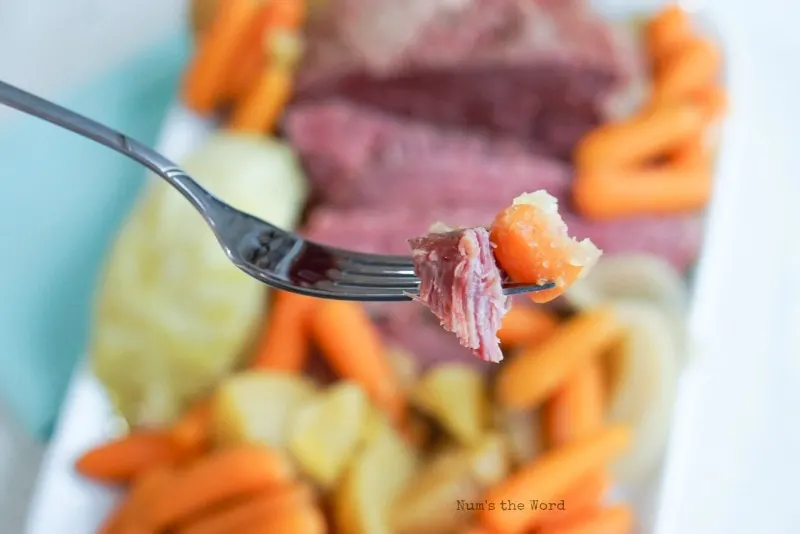 Corned Beef & Cabbage - Corned beef with vegetables on platter in background. Fork with carrot & corned beef in foreground