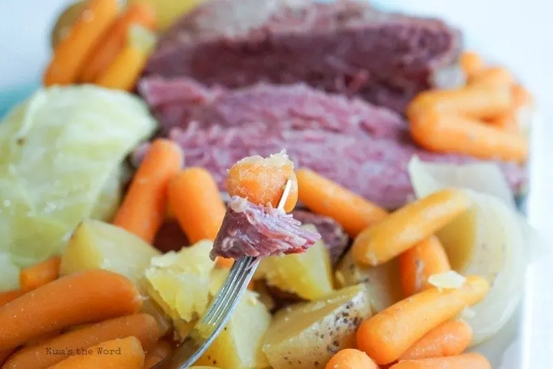 Corned Beef & Cabbage - second angle of corned beef & cabbage in background with fork spearing corned beef and carrot in foreground.