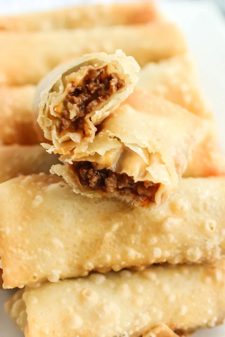 cooked taco egg rolls on a platter to serve with one cut in half to show filling inside.