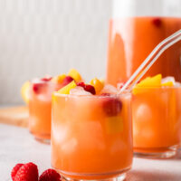 side view of 2 drinks in glasses with a pitcher of lemonade in the background.