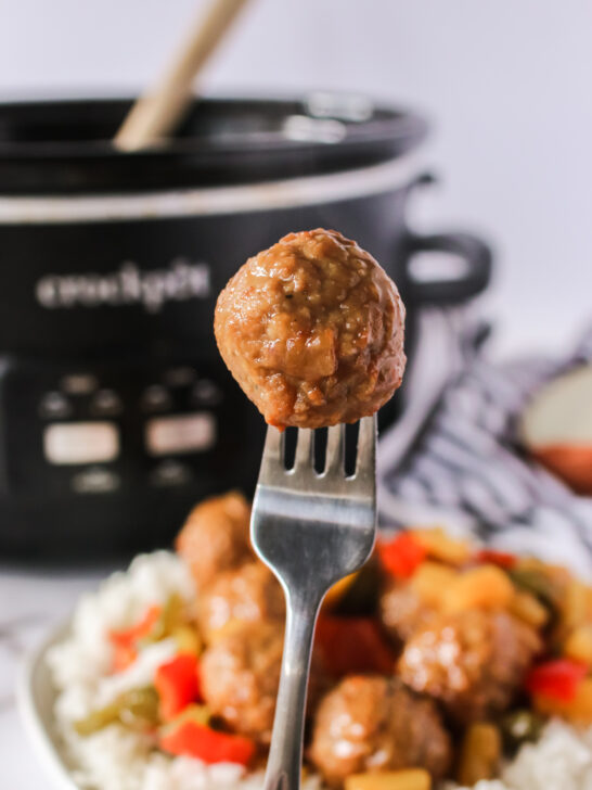 bed of meatballs on rice with a fork holding up a meatball and slow cooker in background