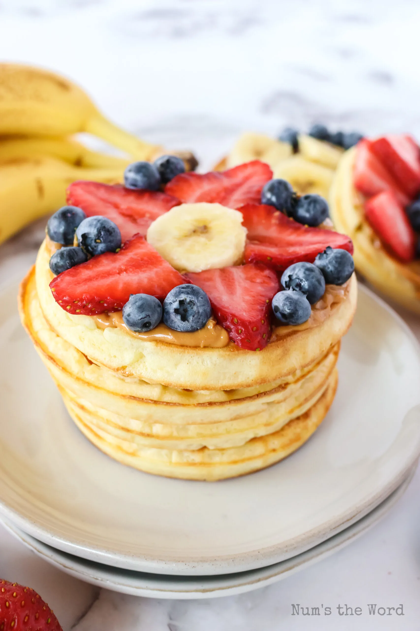 Top side view of 3 waffles. Top one has strawberries, blueberries and a banana slice