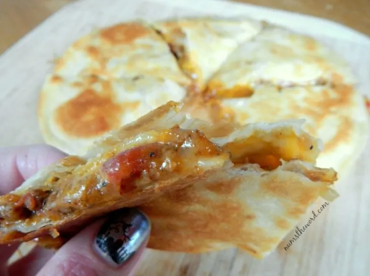 Mexican Quesadilla - cooked and sliced quesadilla. Fingers holding a slice up showing off tasty insides.