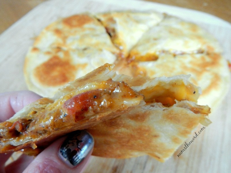 Mexican Quesadilla - cooked and sliced quesadilla. Fingers holding a slice up showing off tasty insides.