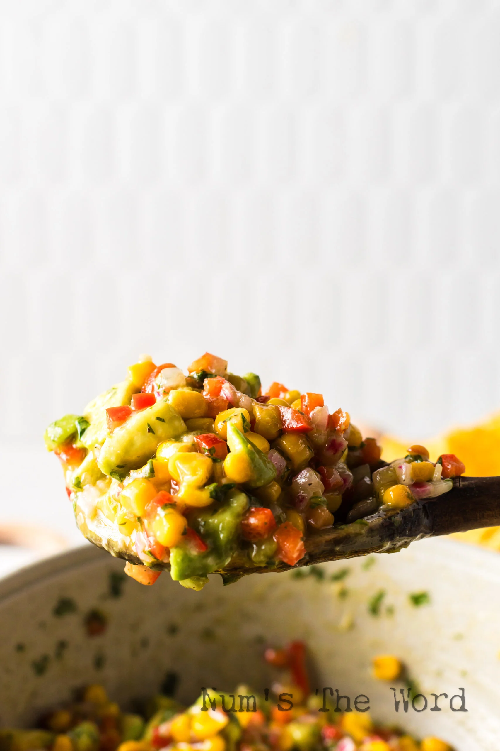 side view of wooden spoon scooping avocado salsa out of bowl .