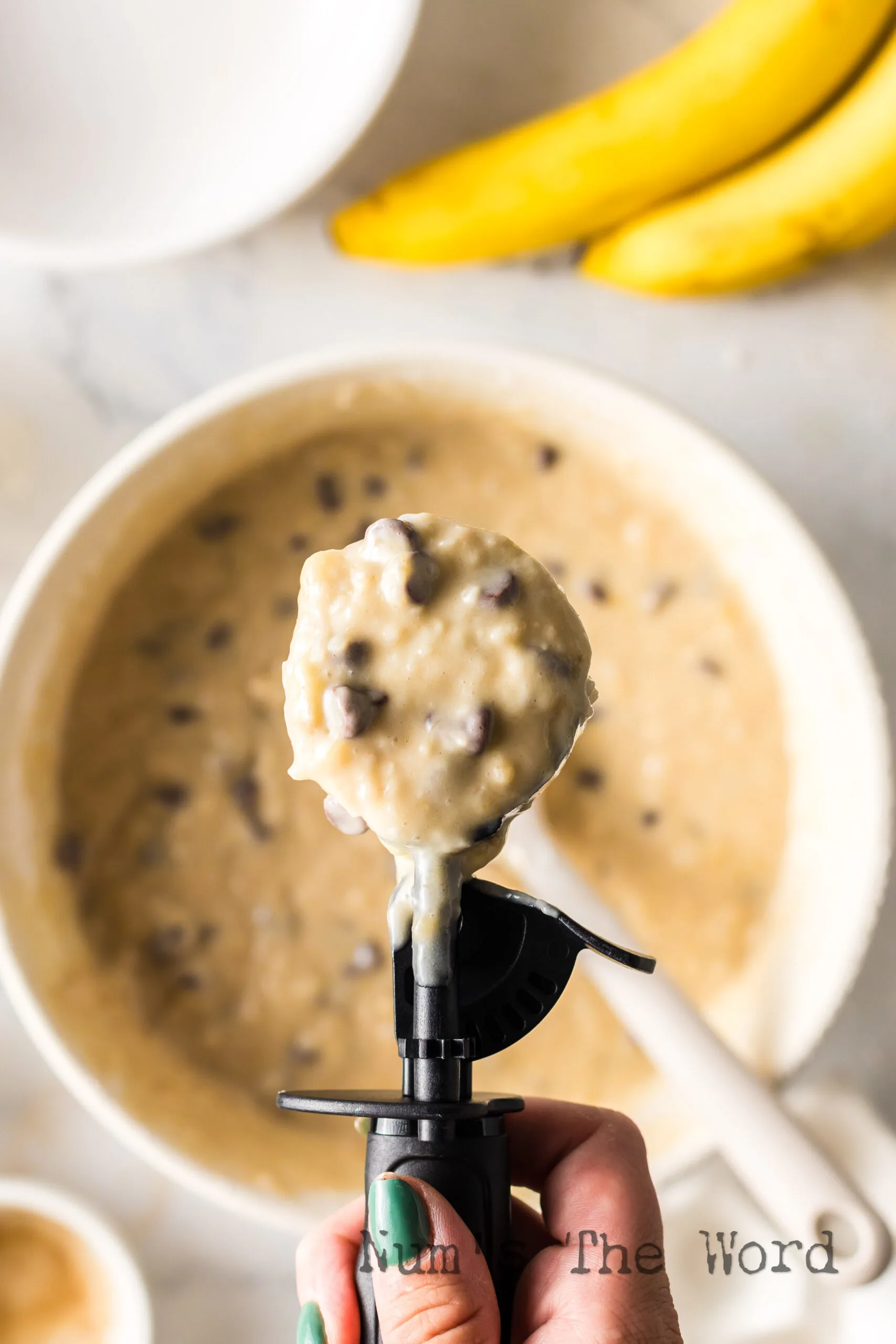 muffin batter mixed in a bowl with a cookie scoop, scooping some out of the bowl.
