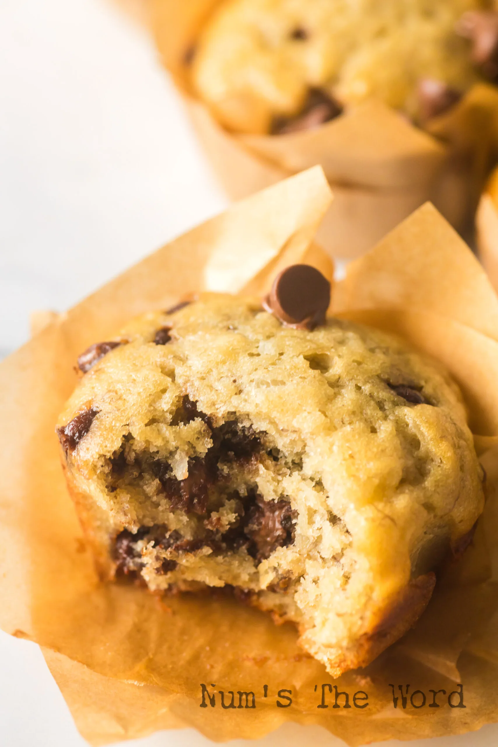 zoomed in image of muffin on counter with a bite removed. Additional muffins in background.