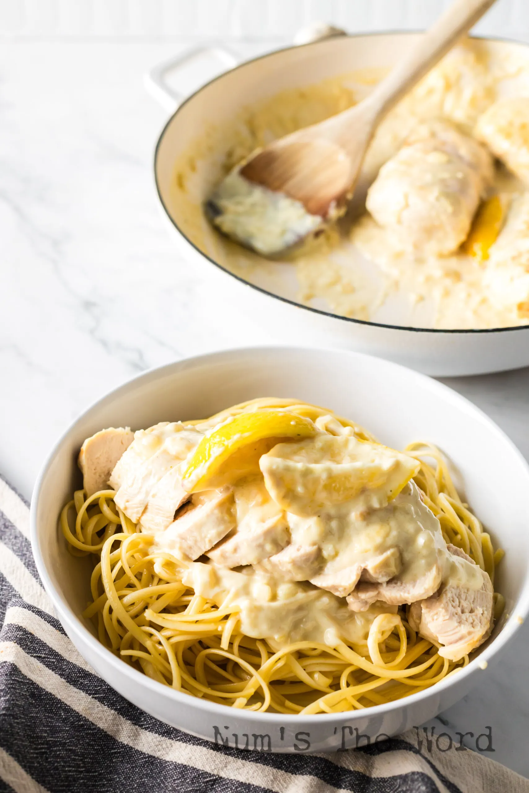 zoomed out image of pasta in bowl with sliced chicken and cream sauce poured over the top.