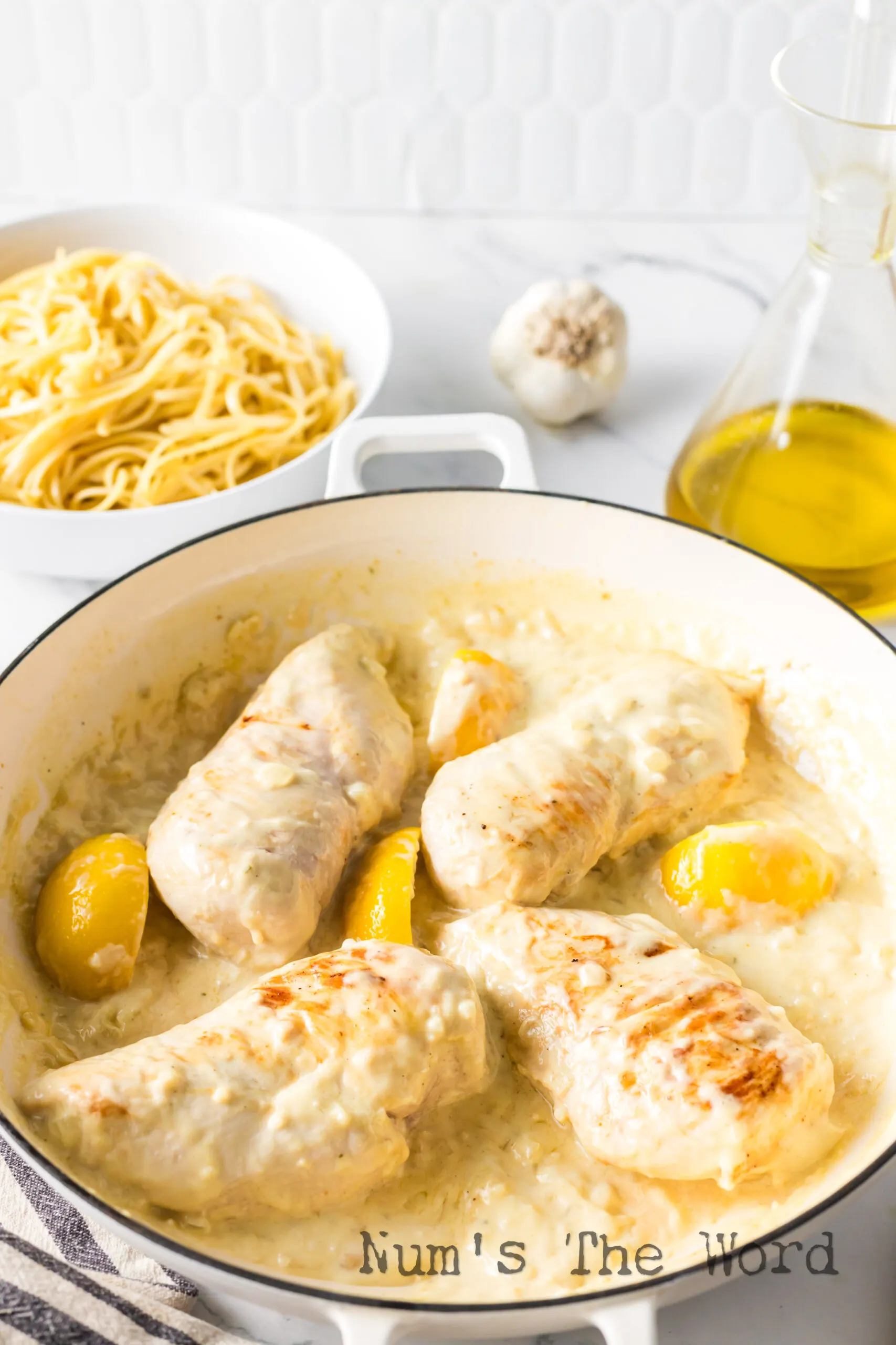 Chicken breasts in skillet with cream sauce and lemon slices.