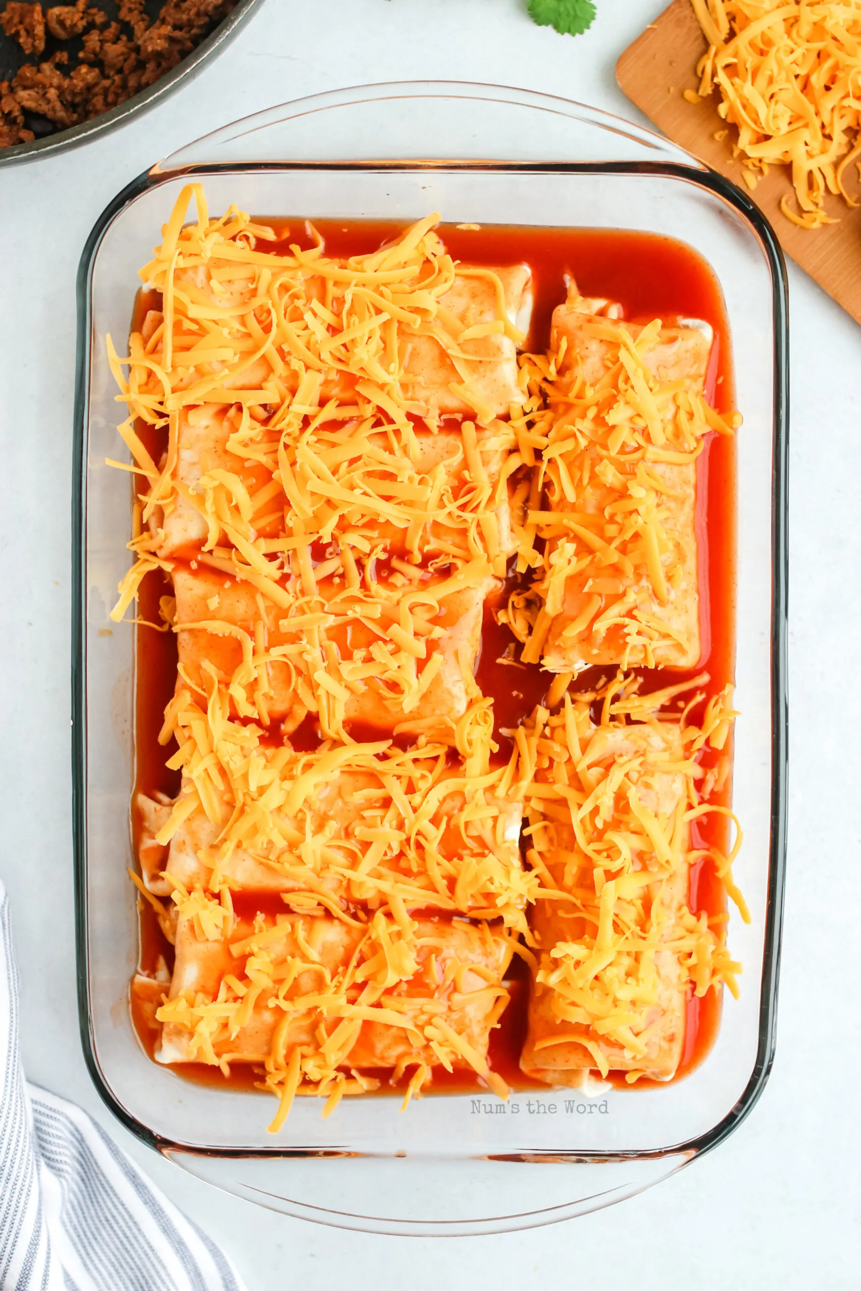 shredded cheese spread on top of baked burritos. ready for oven.