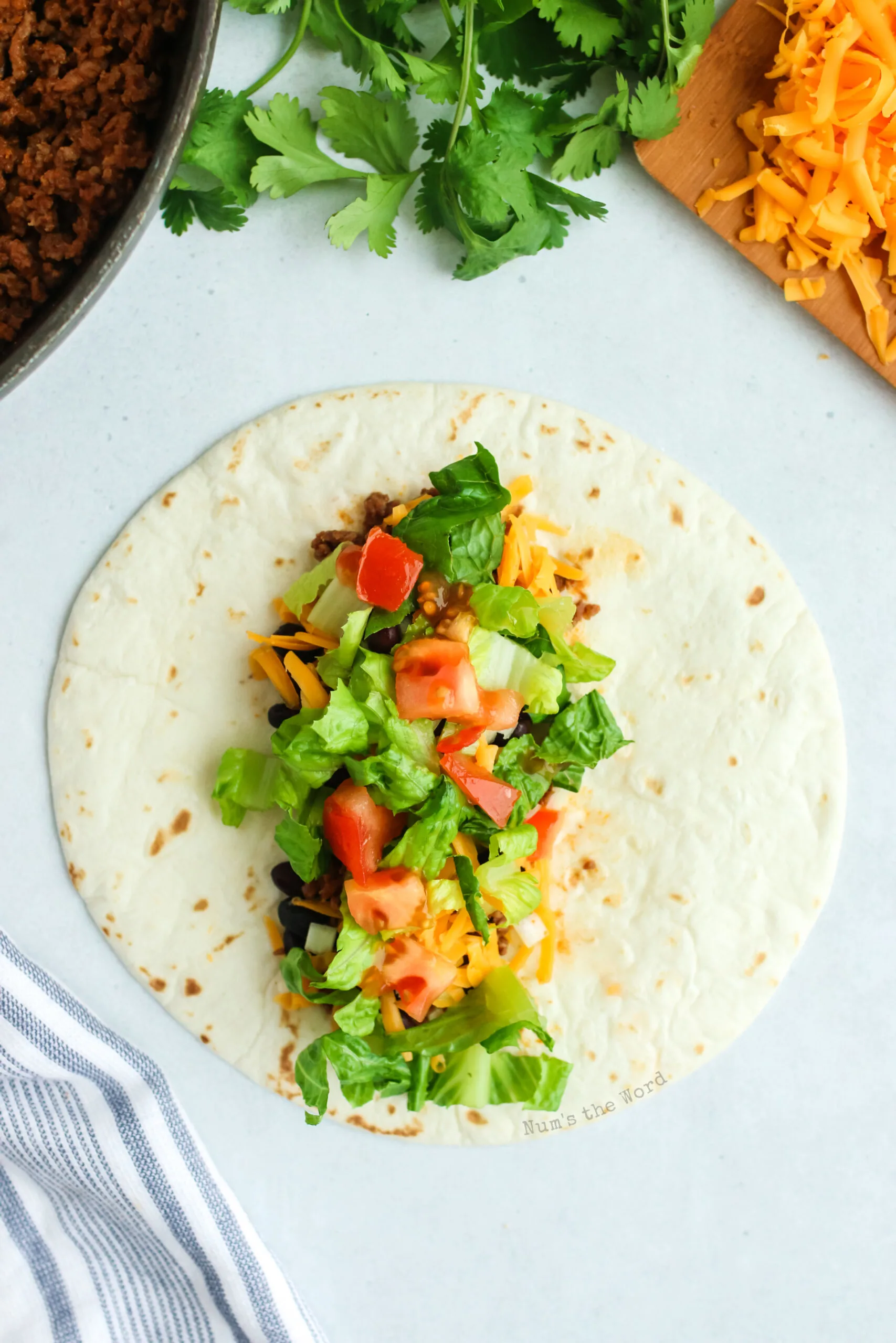 tortilla laying flat with ground beef, lettuce, tomatoes and cheese piled inside.