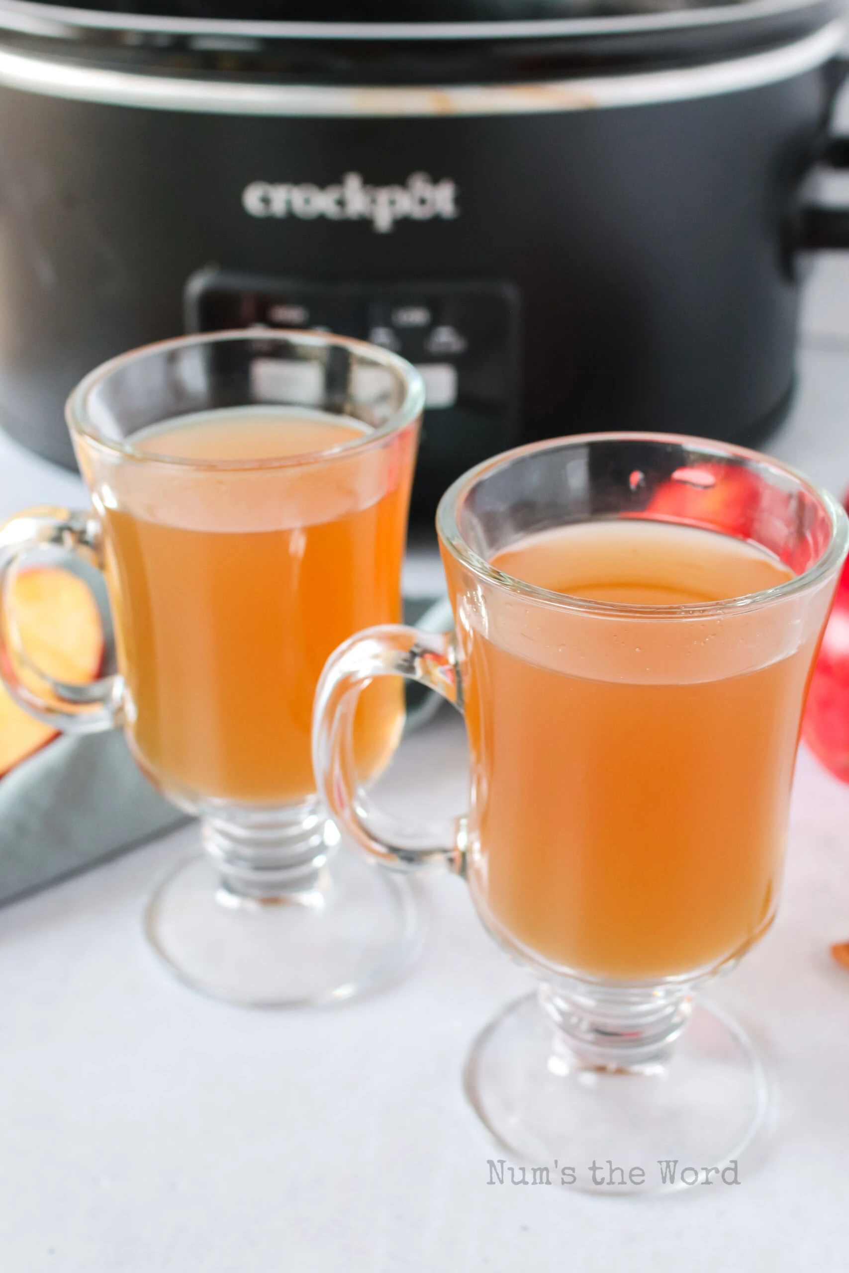 2 glasses of apple cider with crock pot in background.