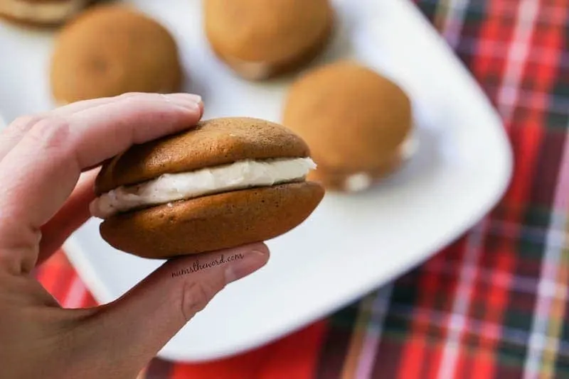 Soft Gingerbread Whoopie Pies - platter of whoopie pies in background, hand holding single whoopie pie close to camera lens.