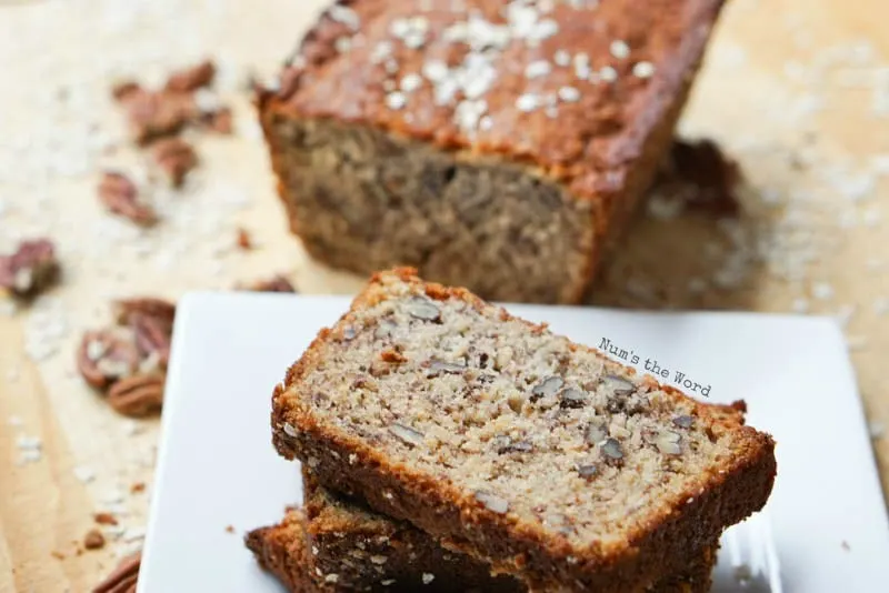 Oatmeal Pecan Banana Bread - Down side angle of sliced bread stacked on plate with half of loaf in background