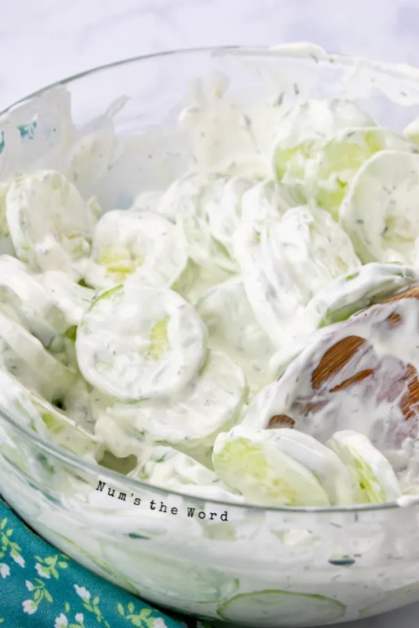 Spoon mixing cucumbers in sauce.