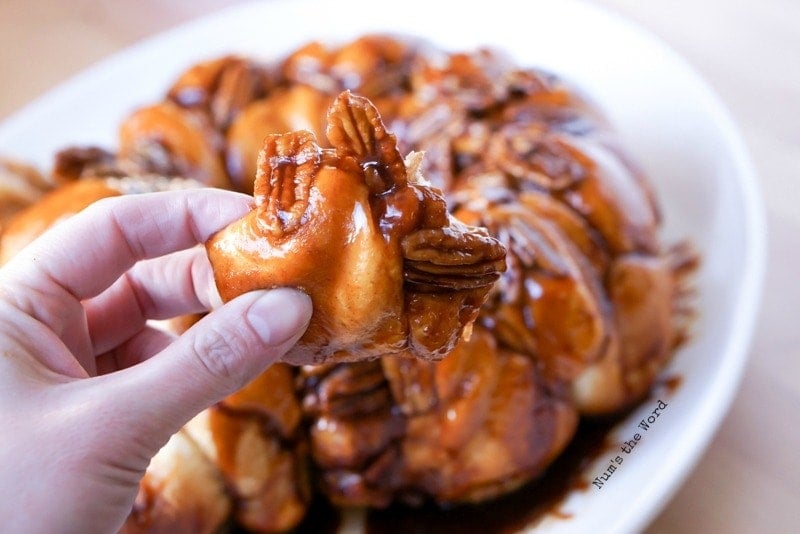 Caramel Pecan Monkey Bread - holding piece of monkey bread in hand covered in caramel and pecans