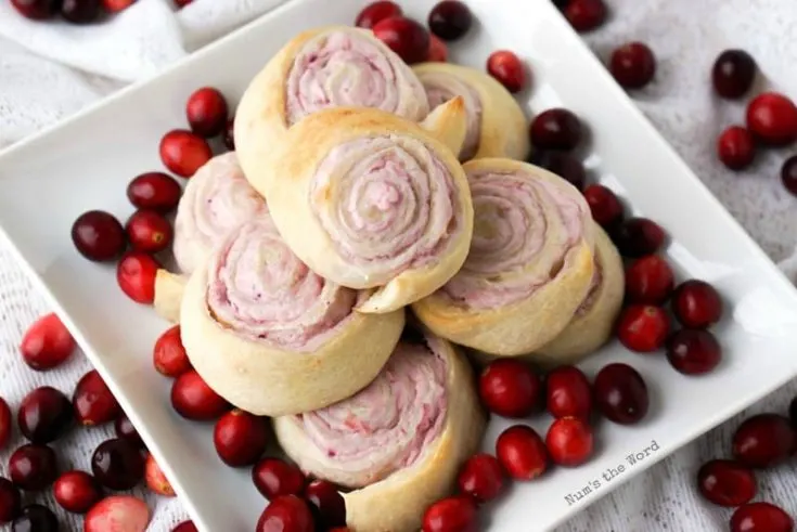 Leftover Cranberry Sauce Roll Ups - Roll Ups stacked on a platter with cranberries all around