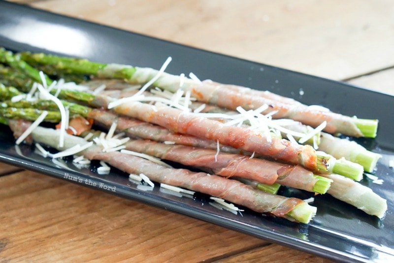Prosciutto Wrapped Asparagus - cooked asparagus on serving tray with Parmesan cheese sprinkled on top.