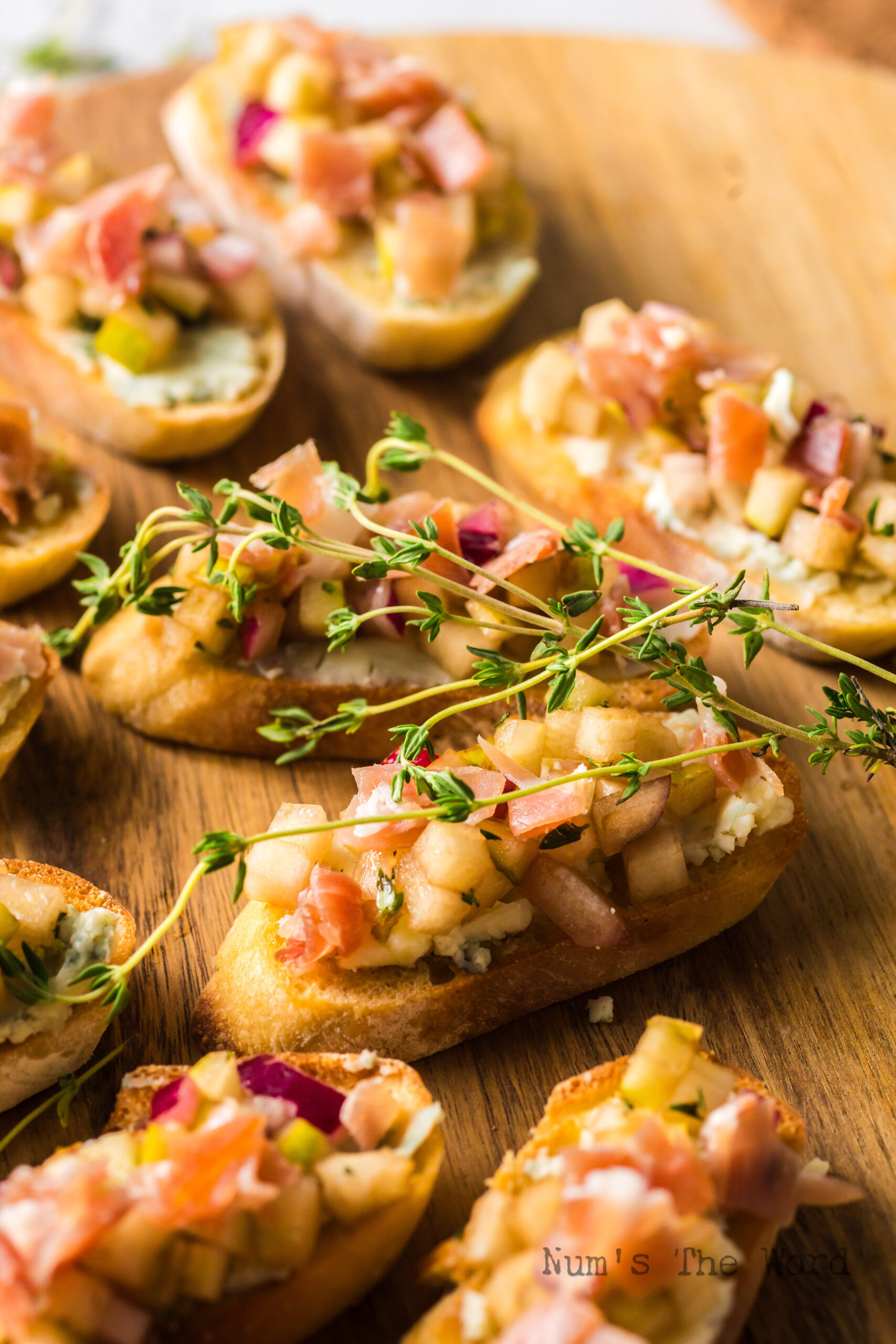 zoomed in image of pear and prosciutto bruschetta on serving tray with sprigs of thyme.
