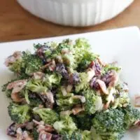 Broccoli salad on a plate with a bow of it behind.