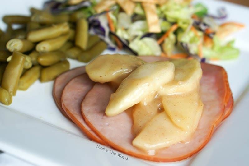 Ham Steaks with Sauteed Apples - close up side view of ham steaks with apples on top with green beans and salad in background