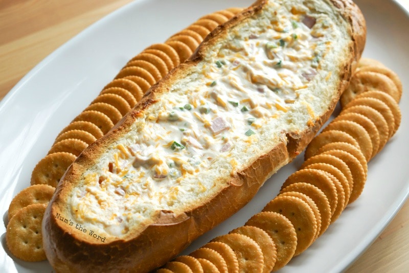 Cheesy Ham Dip in a Bread Bowl - Cooked bread bowl on platter with ritz crackers all around it