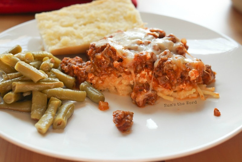 Spaghetti Casserole - side view of casserole on a plate with green beans and garlic bread.