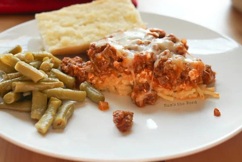 Spaghetti Casserole - side view of casserole on a plate with green beans and garlic bread.