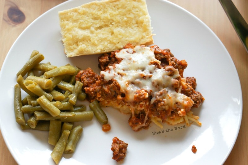 Spaghetti Casserole - casserole on plate with garlic bread and green beans. Photo taken from above.