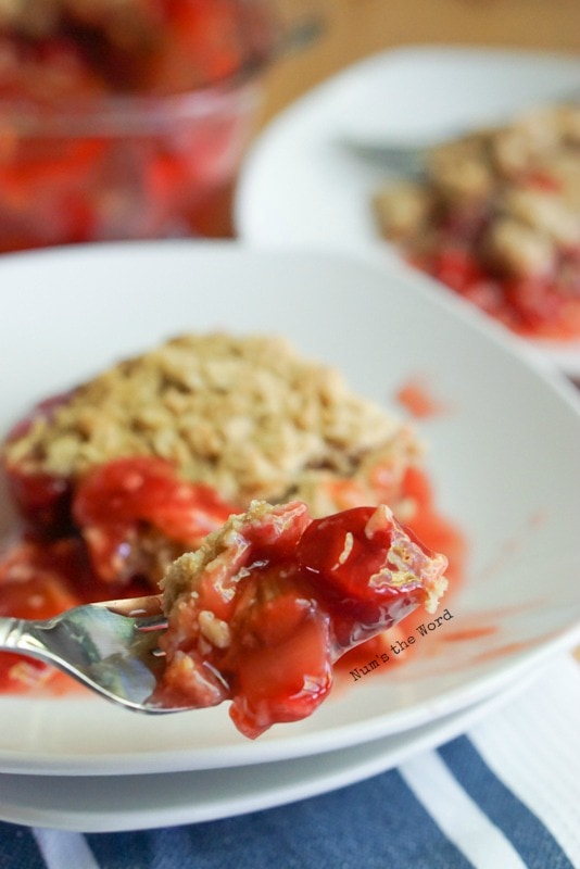 Cherry Rhubarb Crisp - two plates of crisp and pan of crisp in background. Fork full of crisp ready to be eaten.